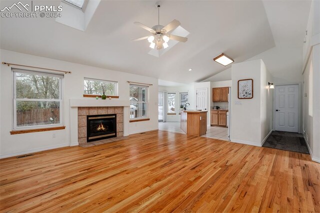 unfurnished living room with a fireplace, light hardwood / wood-style floors, ceiling fan, and lofted ceiling with skylight