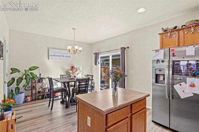 kitchen featuring stainless steel refrigerator with ice dispenser, a center island, decorative light fixtures, a textured ceiling, and light hardwood / wood-style floors