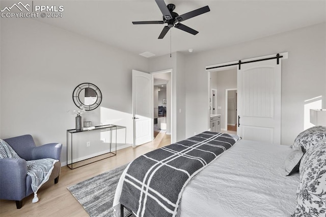 bedroom with ensuite bathroom, light hardwood / wood-style flooring, a barn door, and ceiling fan