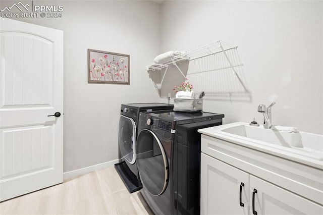 laundry room featuring washer and clothes dryer, cabinets, sink, and light hardwood / wood-style floors