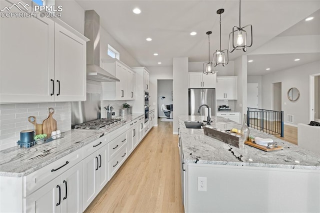 kitchen with wall chimney exhaust hood, sink, white cabinetry, light hardwood / wood-style flooring, and decorative light fixtures