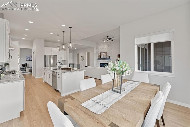 dining room with light wood-type flooring, sink, ceiling fan, and a brick fireplace