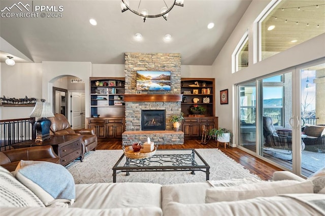 living room with built in shelves, a stone fireplace, lofted ceiling, and wood-type flooring