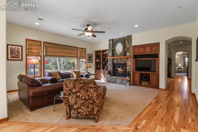 living room featuring ceiling fan, a stone fireplace, and light hardwood / wood-style flooring