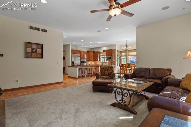 living room featuring ceiling fan with notable chandelier and light hardwood / wood-style floors