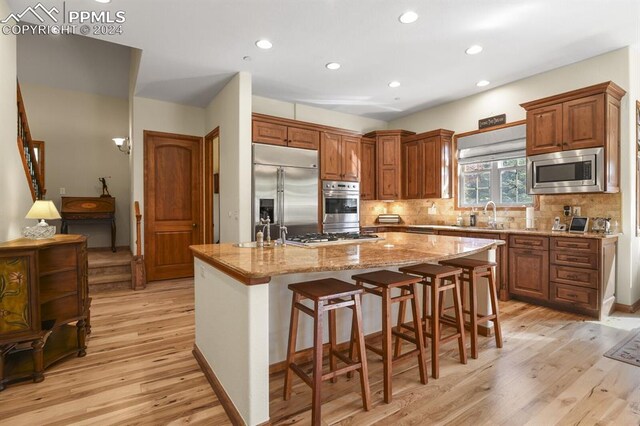 kitchen with built in appliances, a spacious island, light hardwood / wood-style flooring, and a kitchen breakfast bar