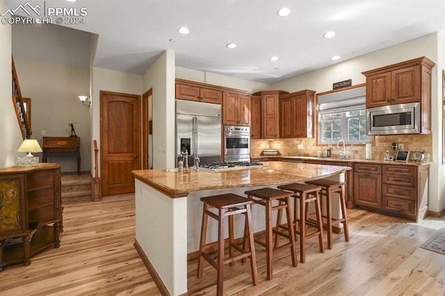 kitchen with built in appliances, decorative backsplash, light wood-style floors, and a kitchen island with sink