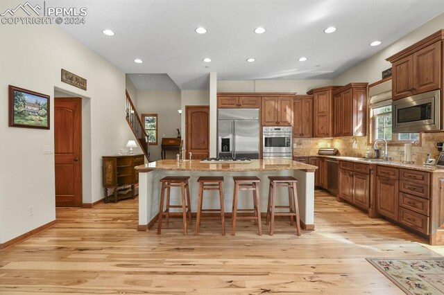 kitchen with a kitchen breakfast bar, built in appliances, light hardwood / wood-style flooring, a center island, and light stone countertops