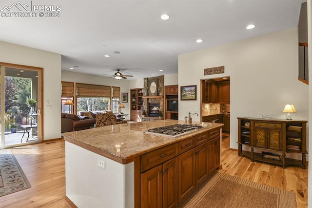 kitchen with light wood-style flooring, recessed lighting, stainless steel gas stovetop, a ceiling fan, and a stone fireplace