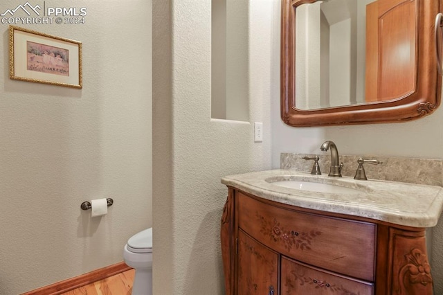 bathroom with toilet, vanity, wood finished floors, and baseboards