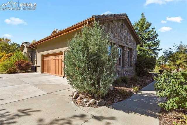 view of home's exterior with concrete driveway, an attached garage, stone siding, and a tile roof