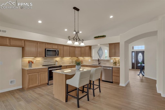 kitchen featuring appliances with stainless steel finishes, sink, a kitchen island, light hardwood / wood-style floors, and pendant lighting