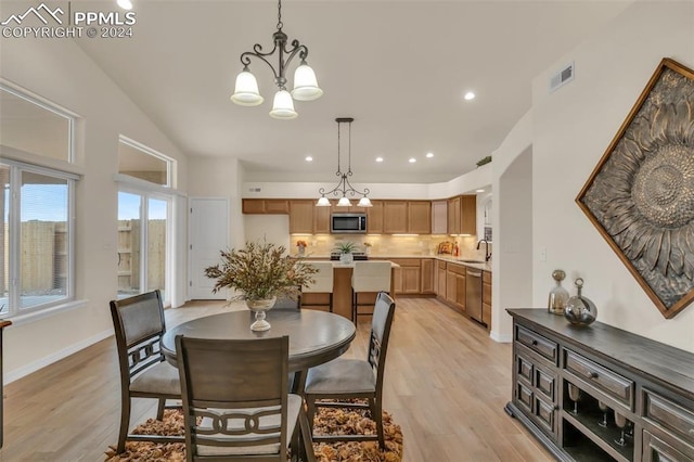 dining area with light hardwood / wood-style floors, an inviting chandelier, sink, and vaulted ceiling