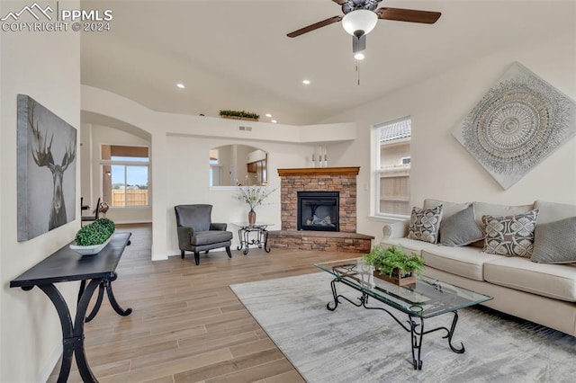 living room with light hardwood / wood-style floors, a stone fireplace, and ceiling fan