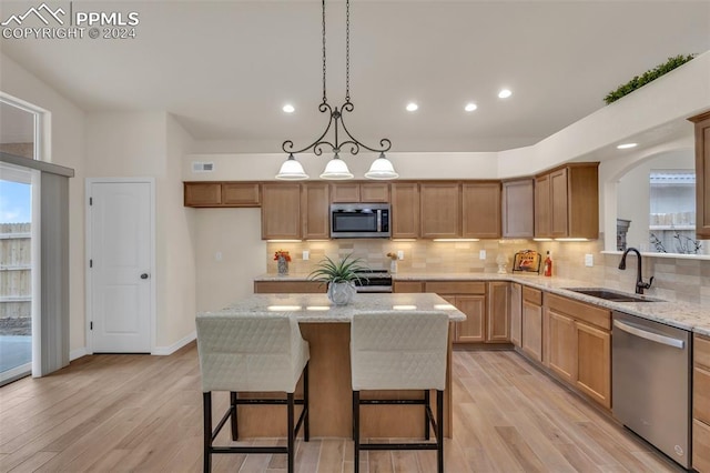 kitchen with light hardwood / wood-style floors, stainless steel appliances, light stone counters, and a kitchen island