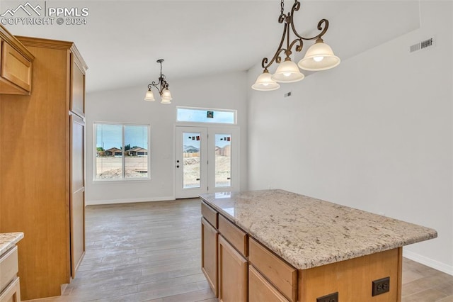 kitchen featuring light stone counters, vaulted ceiling, a center island, light hardwood / wood-style floors, and decorative light fixtures