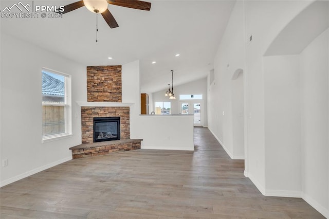 unfurnished living room with lofted ceiling, ceiling fan with notable chandelier, a fireplace, and light wood-type flooring