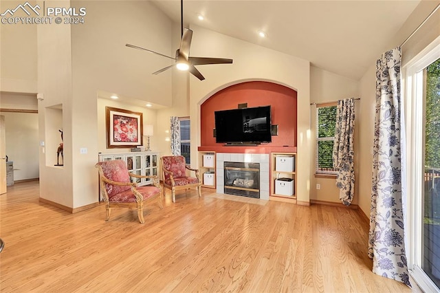 living room featuring a tiled fireplace, light hardwood / wood-style floors, high vaulted ceiling, and ceiling fan