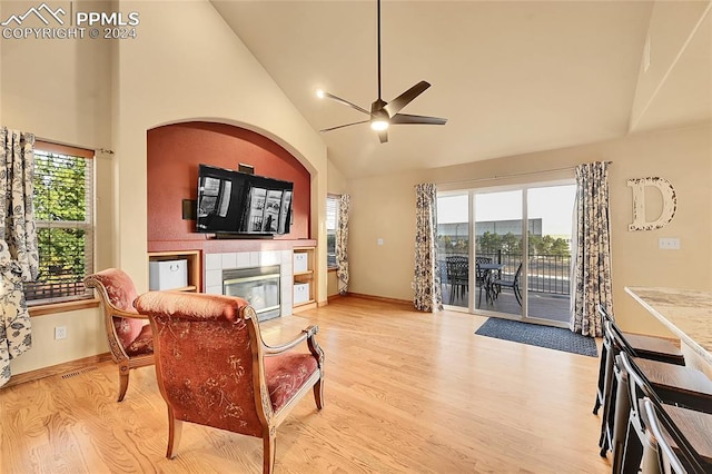 living room featuring light hardwood / wood-style floors, a tiled fireplace, high vaulted ceiling, and ceiling fan