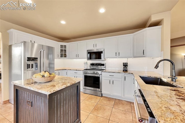 kitchen featuring stainless steel appliances, backsplash, sink, light stone countertops, and white cabinets