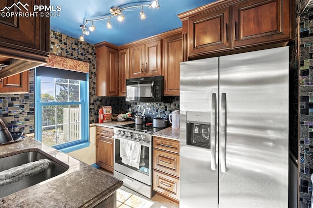 kitchen with decorative backsplash, rail lighting, appliances with stainless steel finishes, dark stone counters, and sink