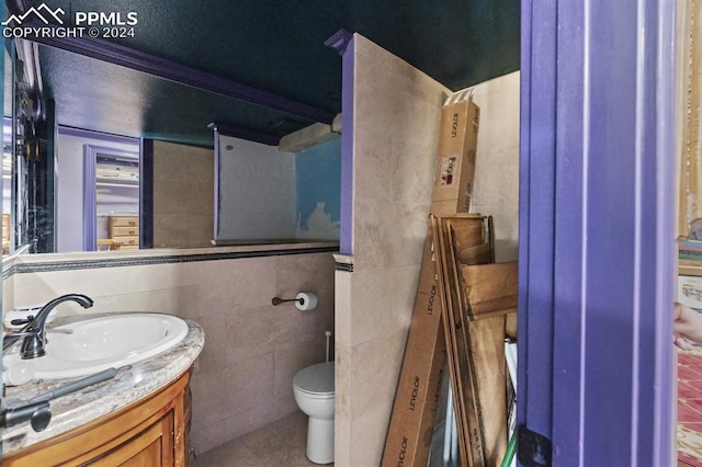 bathroom with tile walls, vanity, toilet, and tile patterned floors