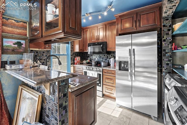 kitchen featuring tasteful backsplash, appliances with stainless steel finishes, dark stone counters, light tile patterned flooring, and sink