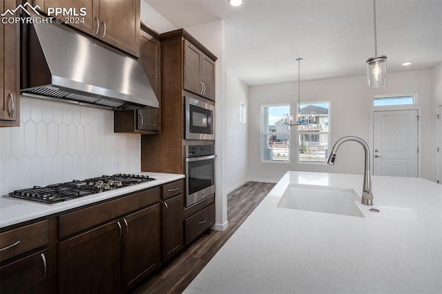 kitchen featuring dark hardwood / wood-style flooring, backsplash, stainless steel appliances, sink, and pendant lighting