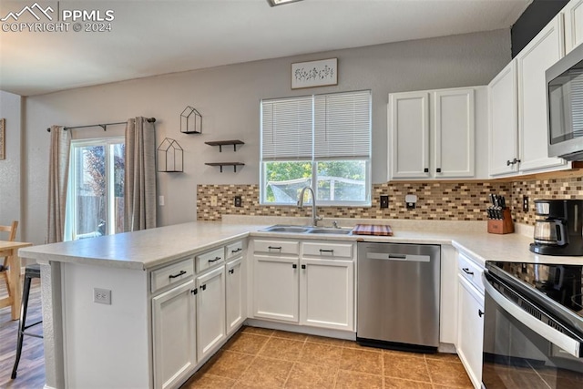 kitchen featuring sink, kitchen peninsula, white cabinetry, stainless steel appliances, and decorative backsplash