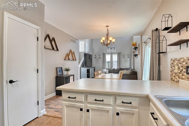 kitchen with hanging light fixtures, kitchen peninsula, light wood-type flooring, a chandelier, and white cabinets