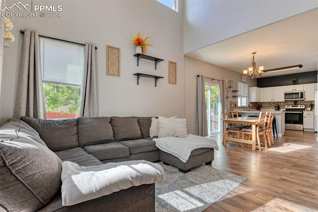 living room with an inviting chandelier, sink, light wood-type flooring, and a high ceiling