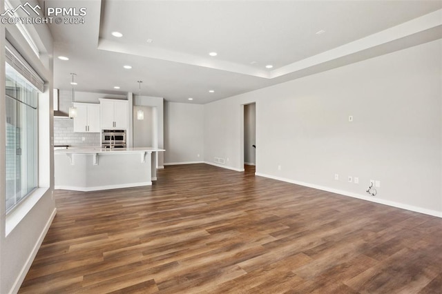 unfurnished living room with a tray ceiling, dark hardwood / wood-style floors, and a healthy amount of sunlight