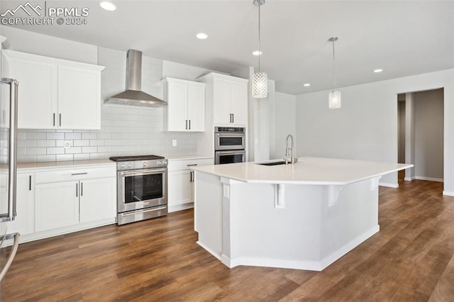 kitchen featuring wall chimney range hood, appliances with stainless steel finishes, sink, an island with sink, and white cabinetry