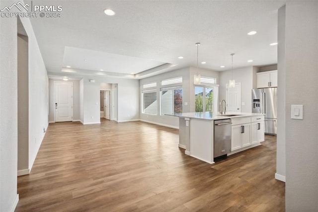 kitchen with appliances with stainless steel finishes, sink, hardwood / wood-style floors, white cabinetry, and a kitchen island with sink