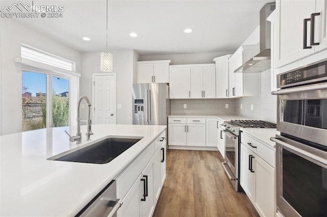 kitchen with appliances with stainless steel finishes, sink, wall chimney exhaust hood, decorative light fixtures, and white cabinets