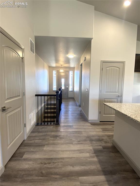 hall with baseboards, visible vents, dark wood-type flooring, and an upstairs landing