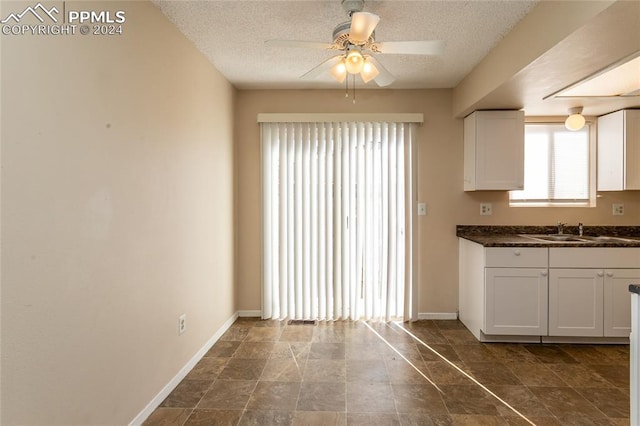 kitchen with a textured ceiling, white cabinets, sink, and ceiling fan