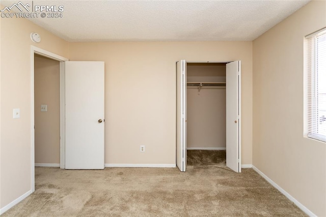 unfurnished bedroom featuring a textured ceiling, light colored carpet, and a closet