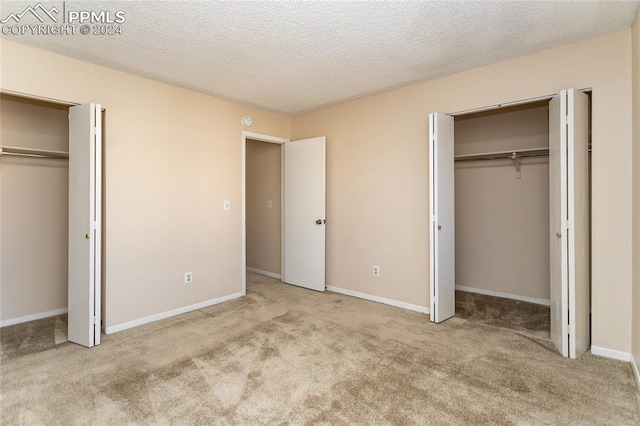 unfurnished bedroom featuring multiple closets, a textured ceiling, and light colored carpet