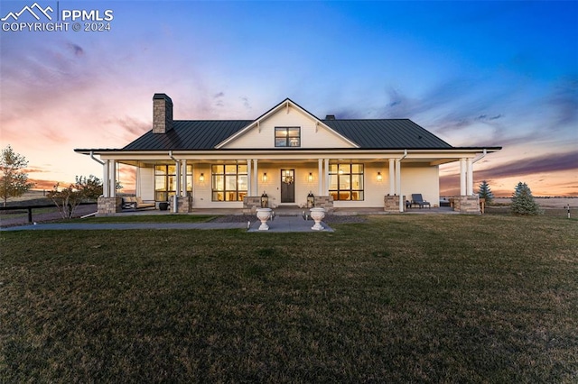 back house at dusk featuring a patio and a lawn