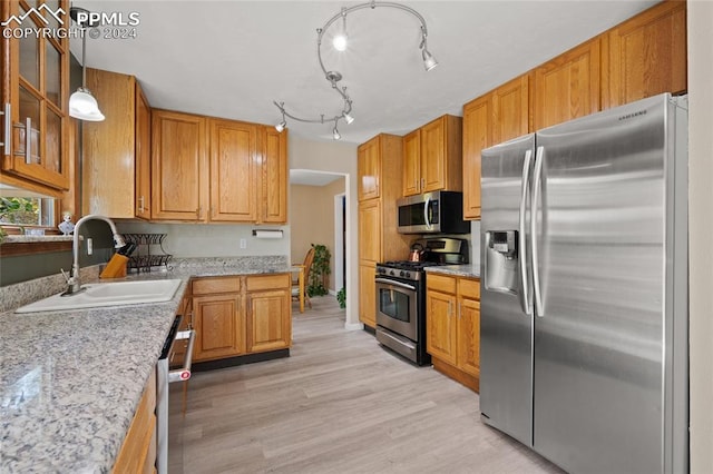 kitchen with stainless steel appliances, sink, decorative light fixtures, light stone counters, and light hardwood / wood-style floors