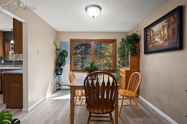 dining room with baseboard heating, sink, light hardwood / wood-style flooring, and a textured ceiling