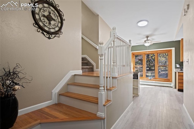 stairs with baseboard heating, wood-type flooring, and ceiling fan