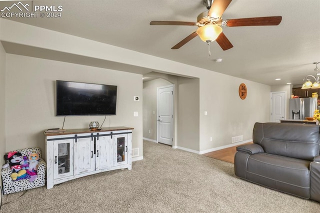 carpeted living room with ceiling fan with notable chandelier