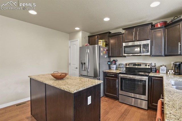 kitchen featuring light stone countertops, a kitchen island, dark brown cabinets, stainless steel appliances, and light hardwood / wood-style flooring