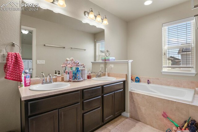 bathroom with vanity, a relaxing tiled tub, a healthy amount of sunlight, and tile patterned flooring