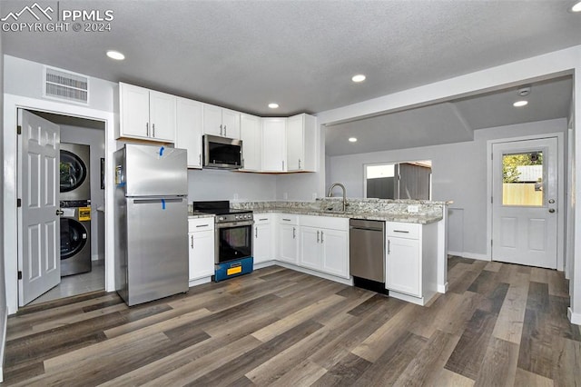 kitchen with sink, stainless steel appliances, white cabinets, stacked washer / drying machine, and dark hardwood / wood-style floors