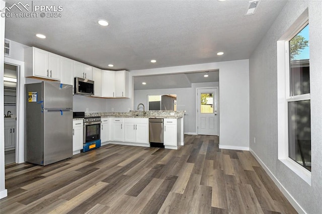 kitchen featuring appliances with stainless steel finishes, sink, white cabinetry, dark wood-type flooring, and light stone counters