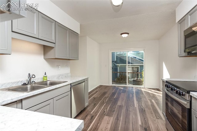 kitchen featuring gray cabinetry, light stone countertops, appliances with stainless steel finishes, sink, and dark wood-type flooring