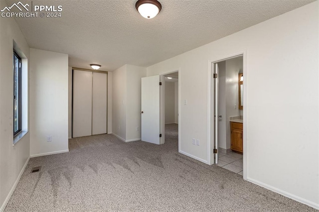 unfurnished bedroom featuring a textured ceiling, light colored carpet, and ensuite bath